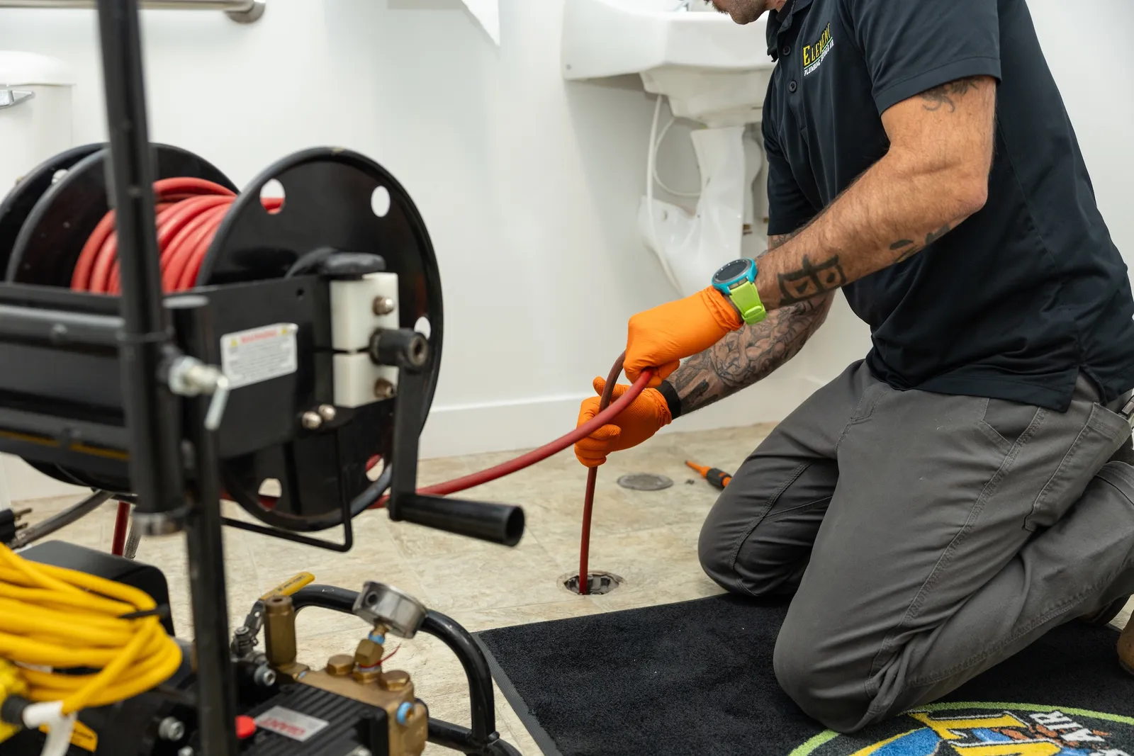Element plumber feeding a hydro-jetting hose into a floor drain to clear an emergency drain clog