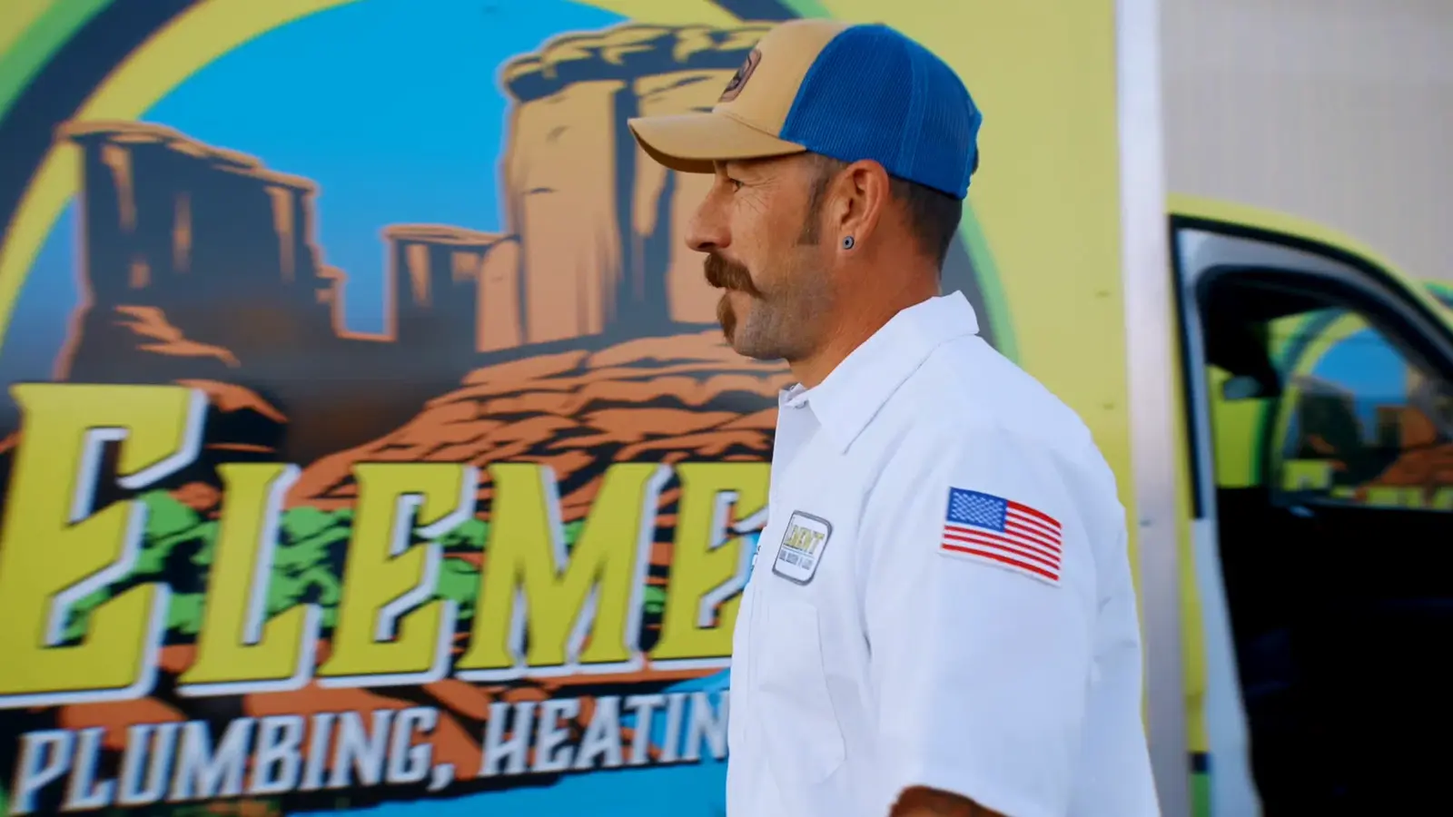 Element plumbing heating air technician in uniform walking past a branded service vehicle with desert landscape graphics in in St. George, UT