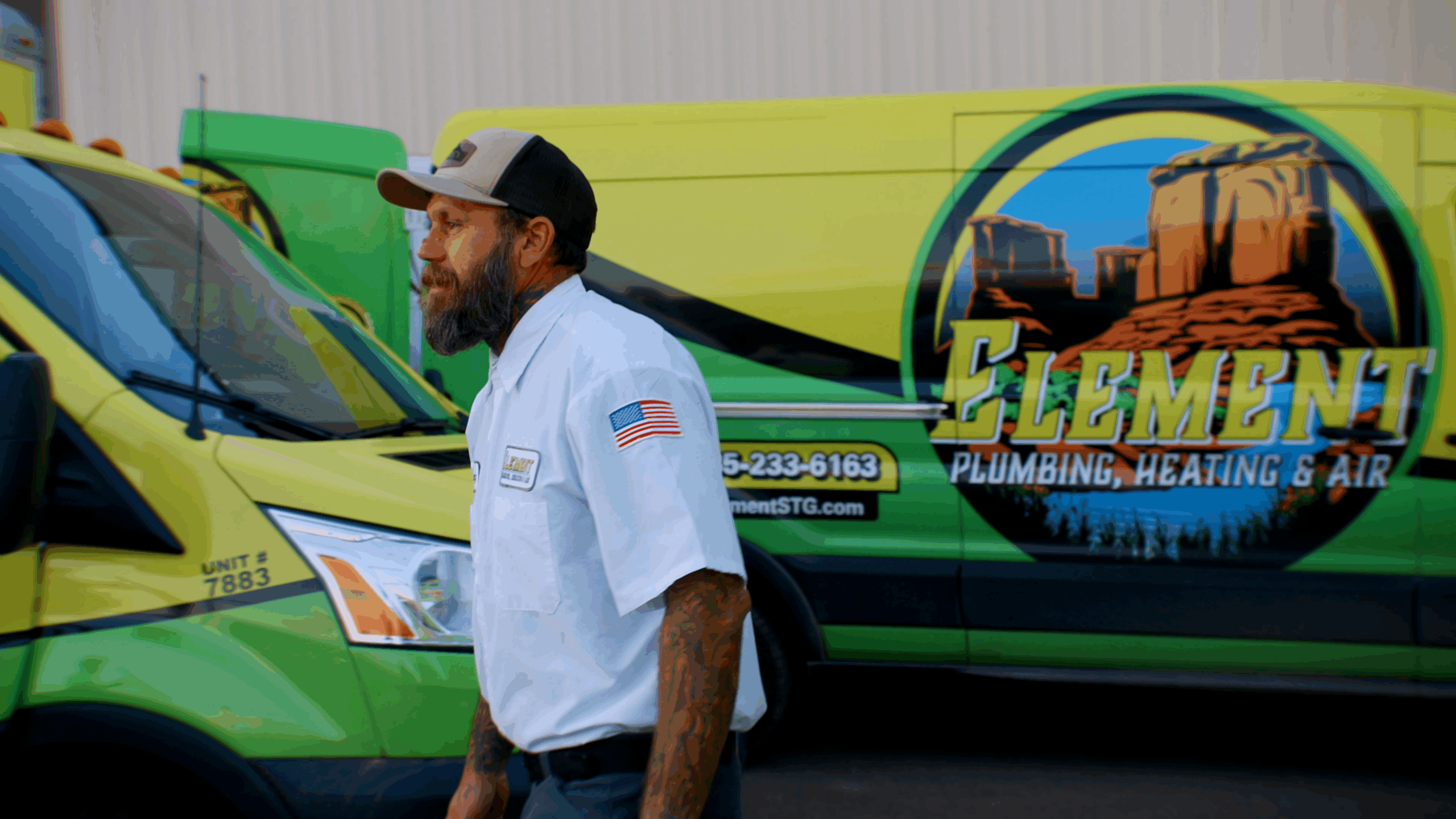 Element Plumbing, Heating & Air technician in uniform walking in front of branded green and yellow service vans with company logo and contact information in St. George, UT.